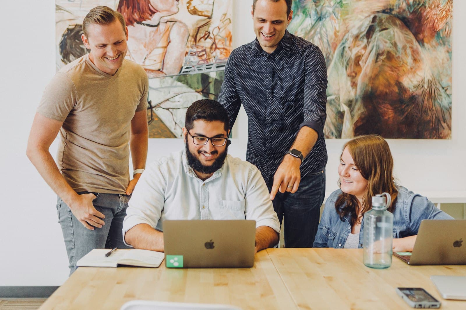 Four colleagues smiling around a laptop at a wooden table